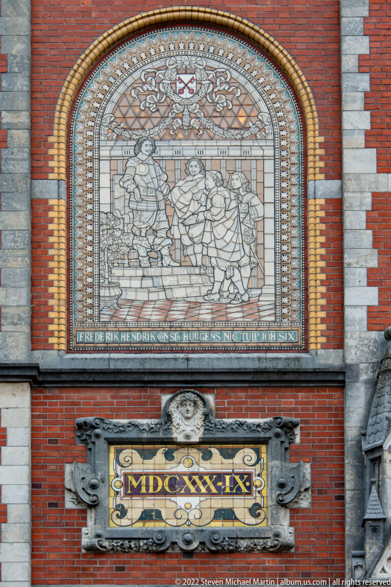Arched historical mosaic and inscription above an ornate cartouche with Roman numerals on the Rijksmuseum façade.