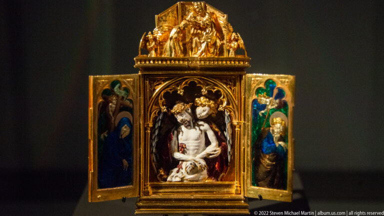 Open gilded triptych with the wounded Christ at center and painted holy figures on two side wings.