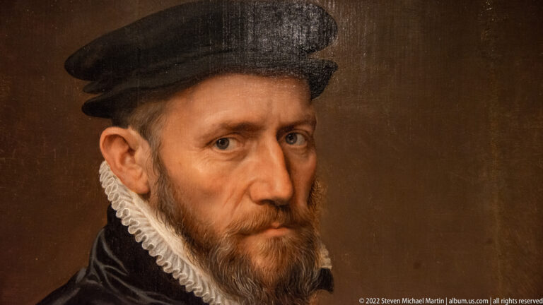 Close portrait of a bearded man in a black cap, dark clothing, and narrow white ruff.