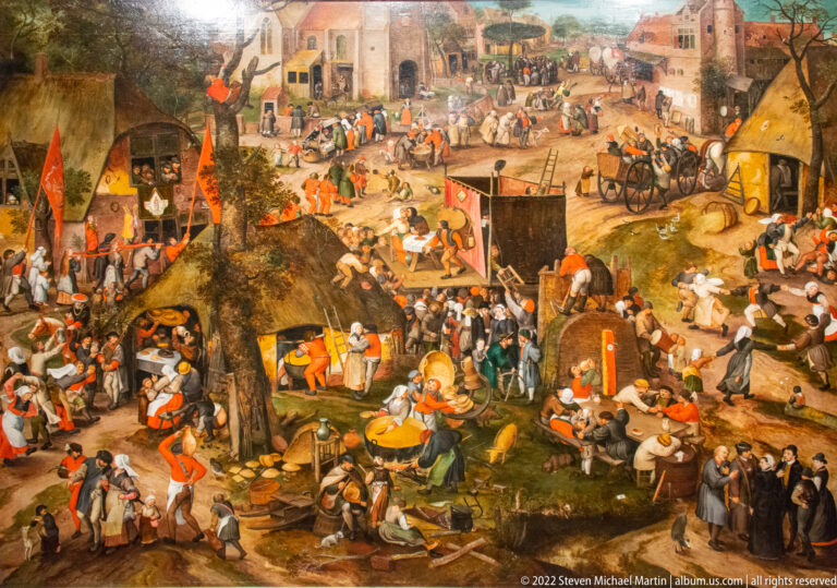 Large village festival scene crowded with dancers, diners, tents, carts, flags, and scattered groups.