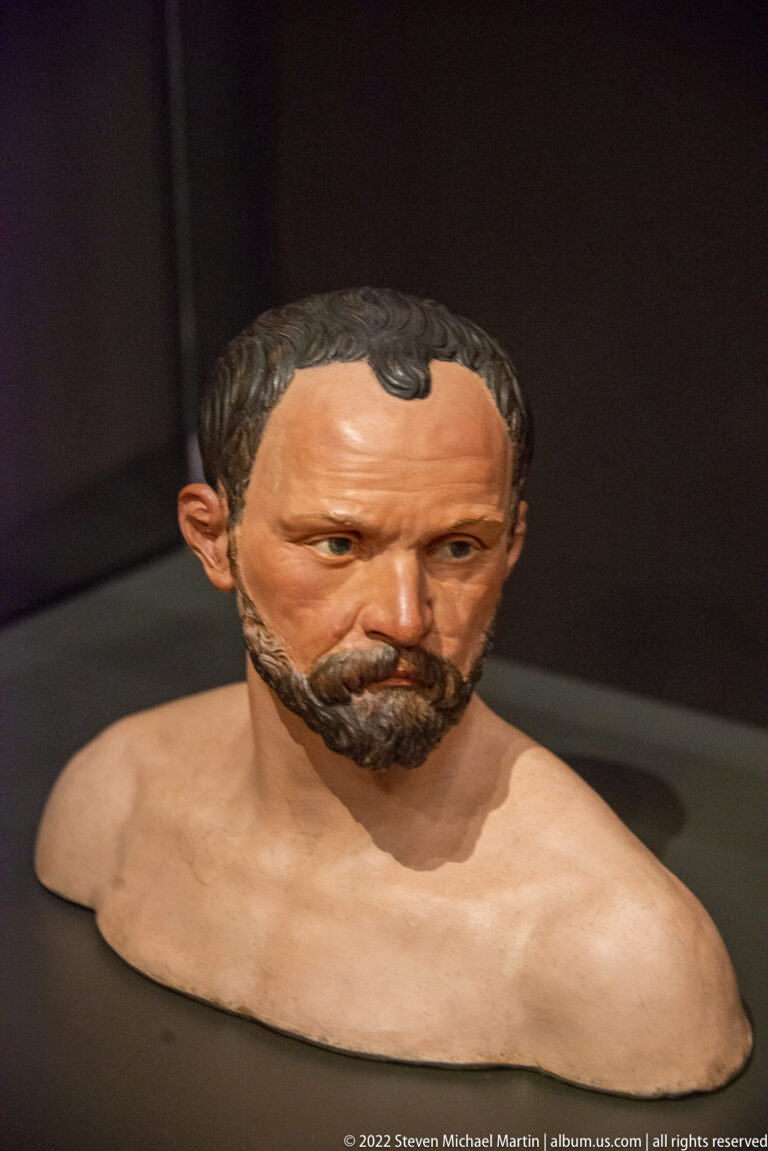 Realistically painted bust of a bearded middle-aged man with bare shoulders and short dark hair.