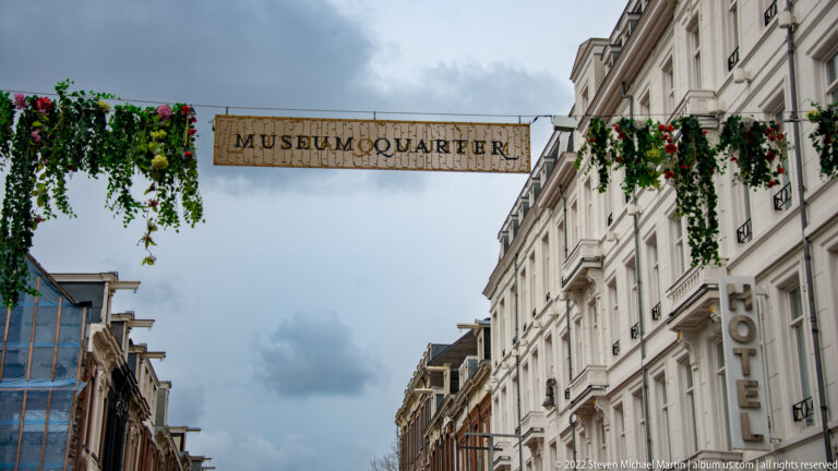 Overhead MUSEUMQUARTIER sign with hanging greenery above a street lined by tall urban buildings.