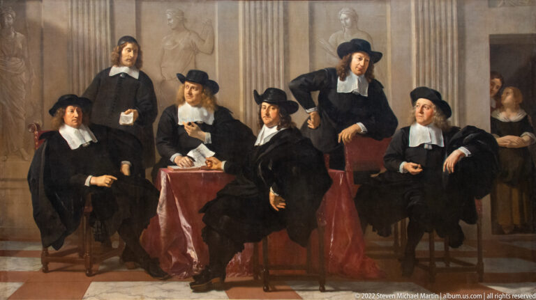 Seven men in black seventeenth-century dress pose around a table in a formal institutional group portrait.