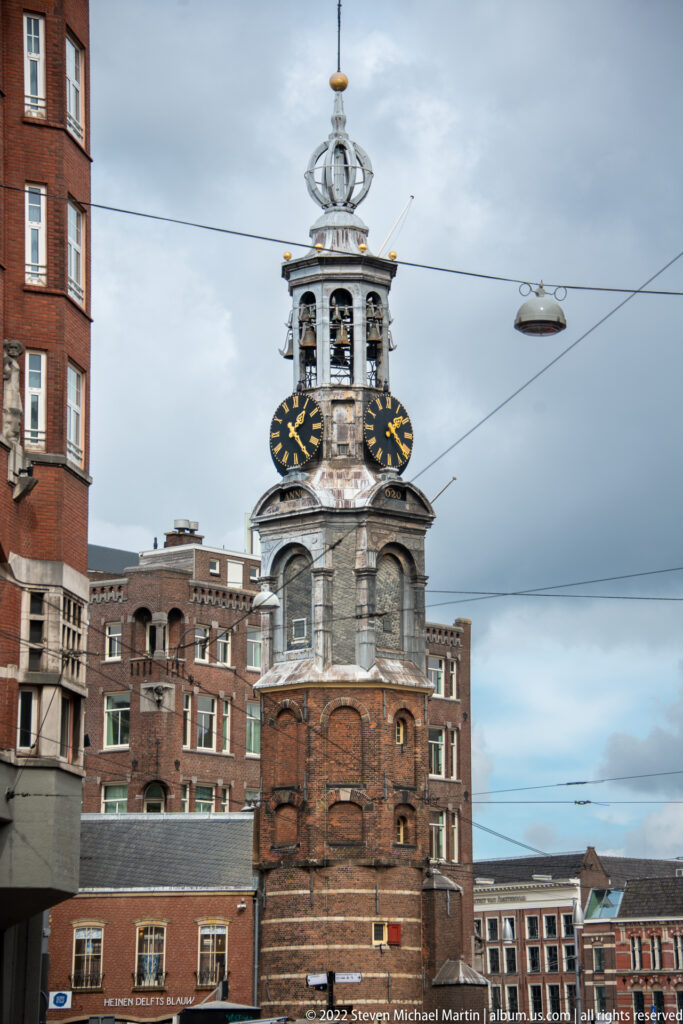 Munttoren clock tower with red-brick base, stone belfry, two black-and-gold clock faces, and open crown.