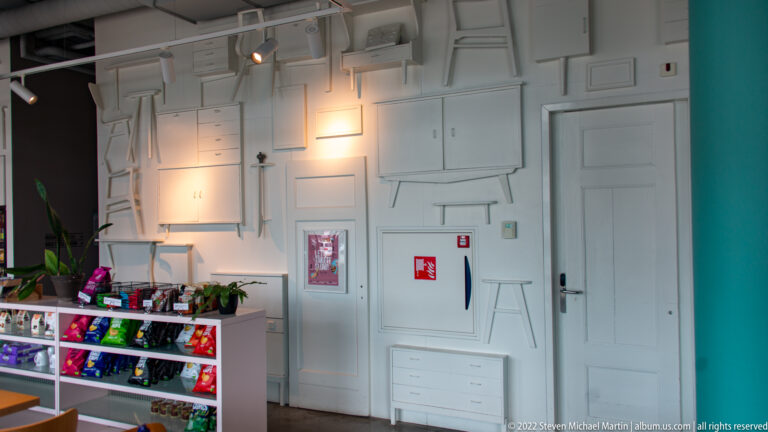 White paneled interior wall with geometric moldings, doors, a small retail display, and turquoise trim.