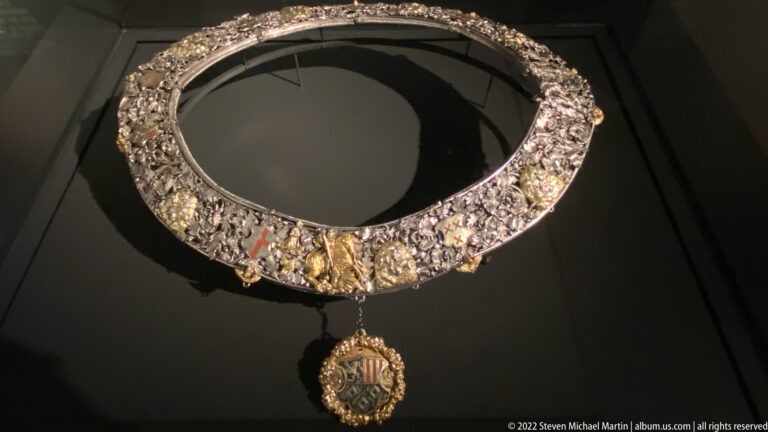 Ornate jeweled ceremonial collar with pearls, colored stones, dense metalwork, and a pendant badge below.