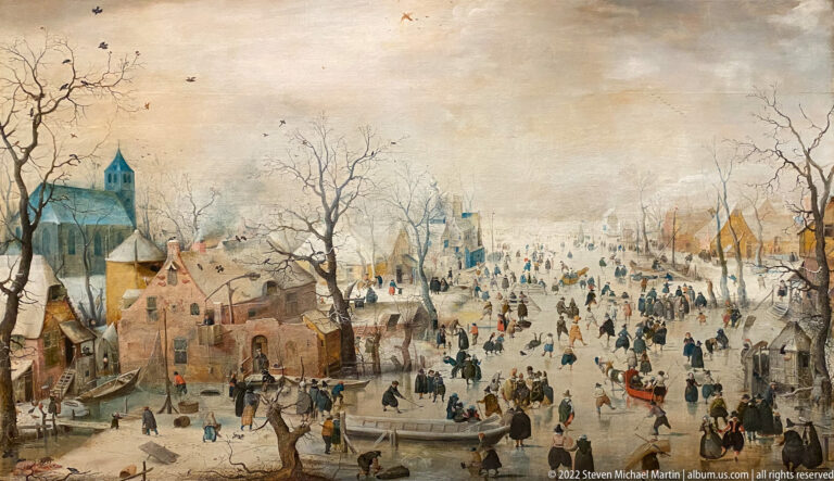 Dutch winter landscape with many skaters on a frozen waterway, village buildings, bare trees, and church towers.