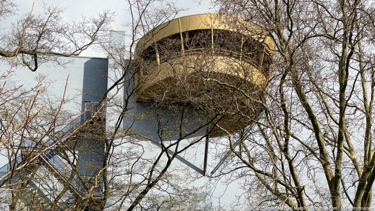 Round elevated pavilion or tower on structural supports, viewed upward through leafless tree branches.