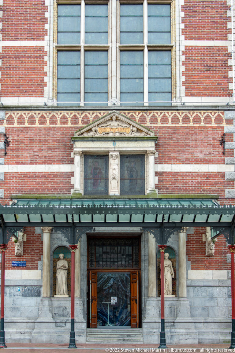 Rijksmuseum doorway beneath a projecting canopy, flanked by sculpted figures in wall niches.