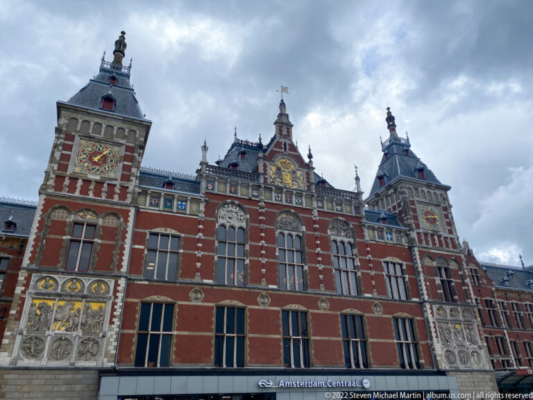Low-angle view of Amsterdam Centraal's ornate red-brick central façade with twin towers, gables, clocks, and station signage.