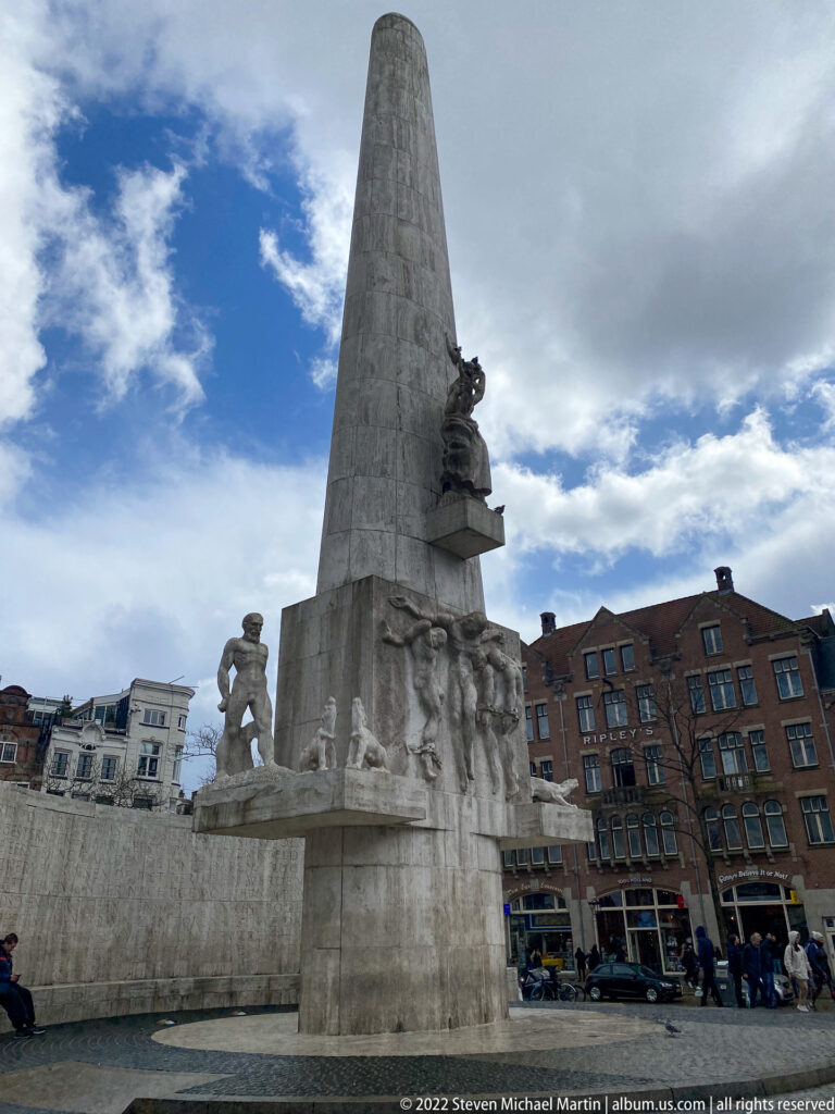 National Monument on Dam Square, a tall pale obelisk with sculpted figures at its base against city buildings.