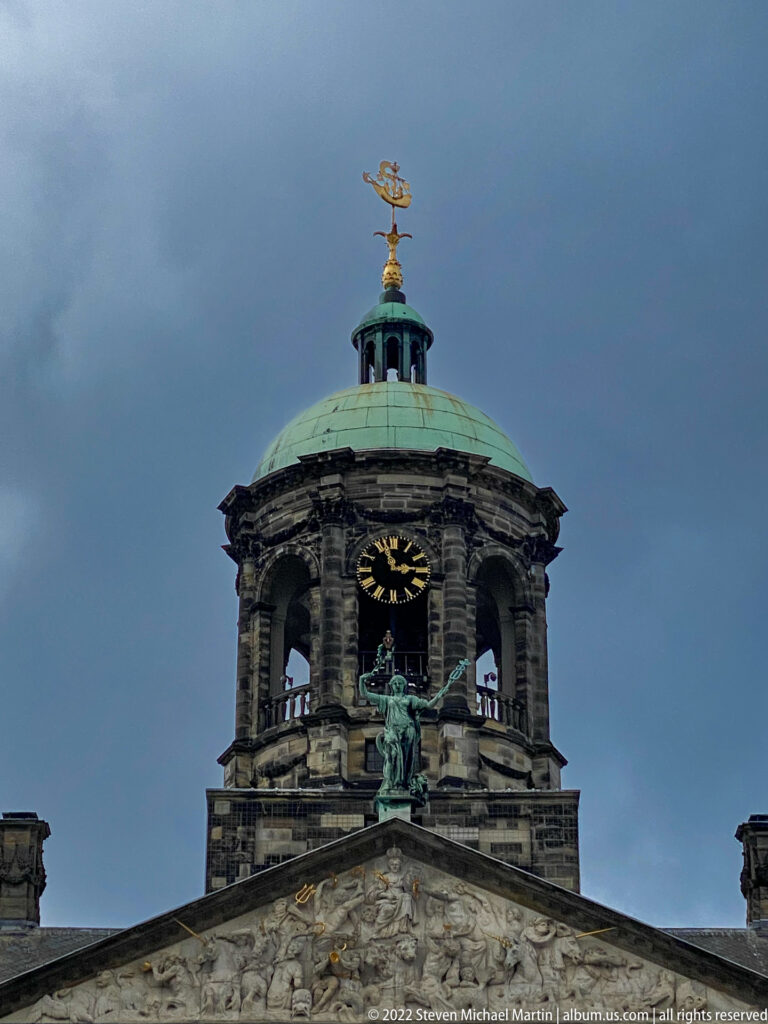 Royal Palace Amsterdam cupola with clock, green-patinated dome, gilded weather vane, and sculptural pediment below.