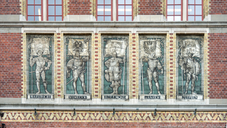 Five vertical Rijksmuseum façade panels with standing figures and city names including Maastricht, Nijmegen, Roermond, Arnhem, and Zutphen.