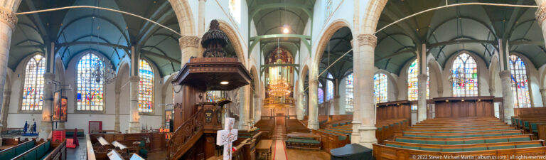 Wide Sint-Janskerk interior with green-cushioned benches, tall columns, stained glass, carved pulpit, and choir.