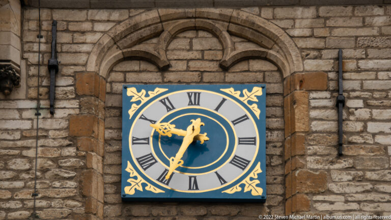 Square blue-and-gold clock with Roman numerals mounted on the stone façade of Gouda Town Hall.