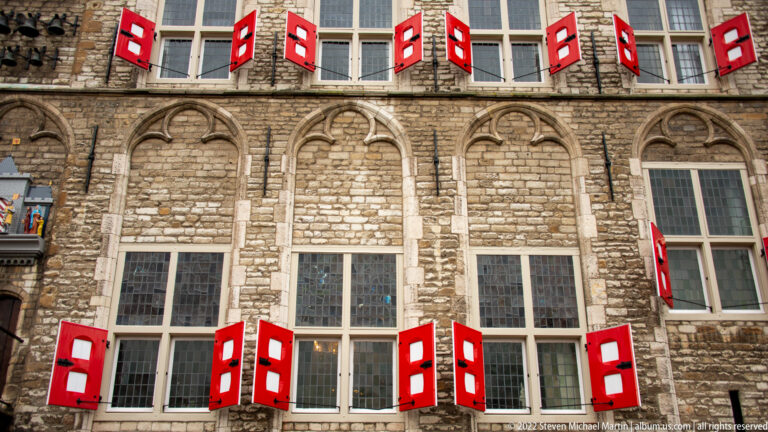 Rows of tall Gouda Town Hall windows with bright red-and-white shutters set in gray stone Gothic arches.