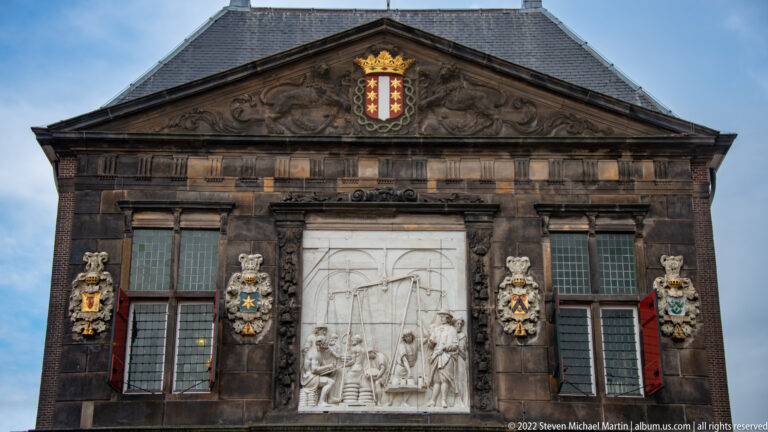Upper façade of the Gouda Waag with triangular pediment, city arms, windows, heraldic shields, and large white relief panel.