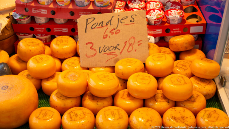 Rows of small orange cheese wheels beneath a handwritten Dutch sign offering “Pondjes 6,50” and three for eighteen euros.