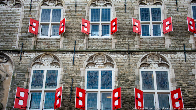 Close façade detail of Gouda Town Hall with two rows of tall windows, carved stone surrounds, and red-white shutters.