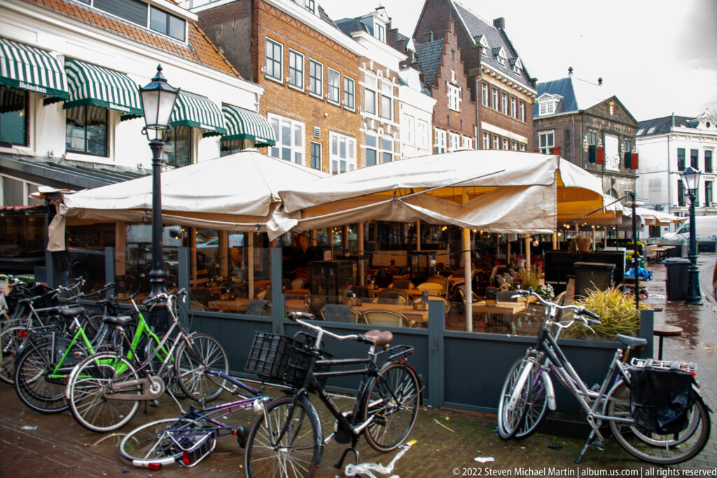 Canvas-covered market stalls and many bicycles on a wet square bordered by historic buildings in central Gouda.