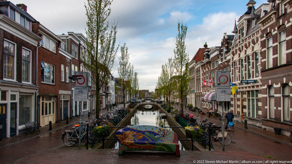Canal lined with brick buildings and bicycles, with a colorful mosaic bench in the foreground.