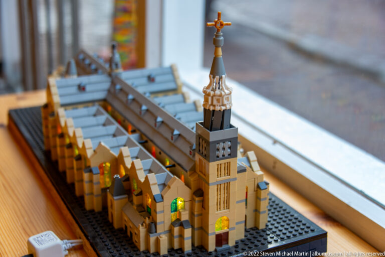 LEGO-style model of an elongated church with square tower, long roof, and colored window inserts.