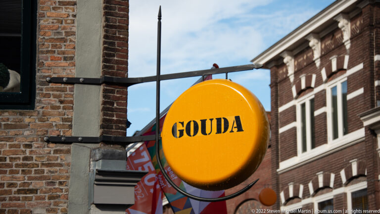 Large round yellow sign resembling a cheese wheel, with GOUDA printed in black letters.