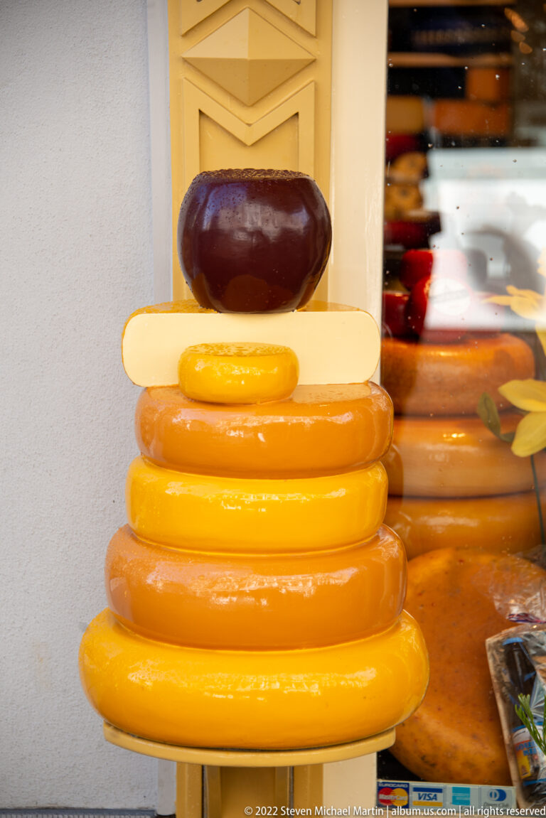 Stacked yellow and orange cheese-wheel forms topped by a pale bar and dark purple sphere.