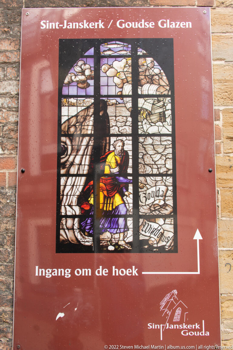 Red Sint-Janskerk and Goudse Glazen visitor sign with stained-glass image and arrow to the entrance.