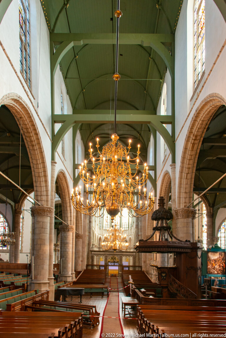 Wide Sint-Janskerk interior with arcades, green roof structure, brass chandeliers, pews, and carved pulpit.