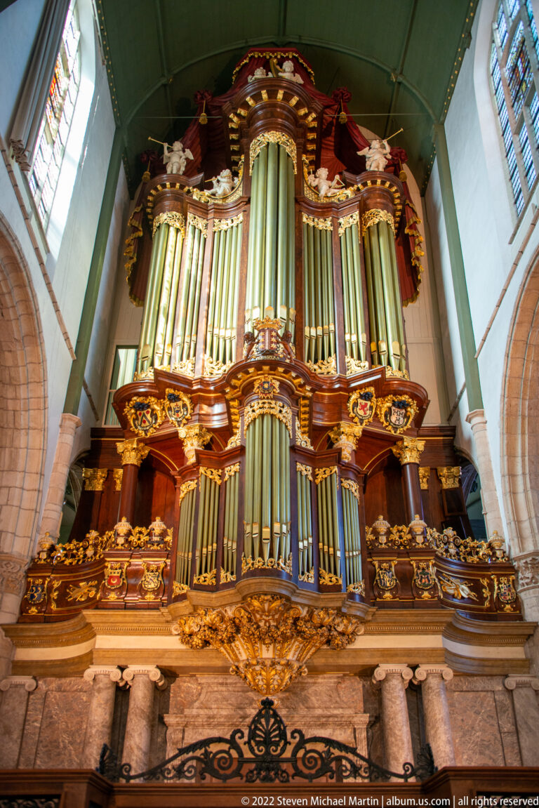 Large ornate pipe organ with silver pipes, dark wood case, gilded carving, and sculptural decoration.