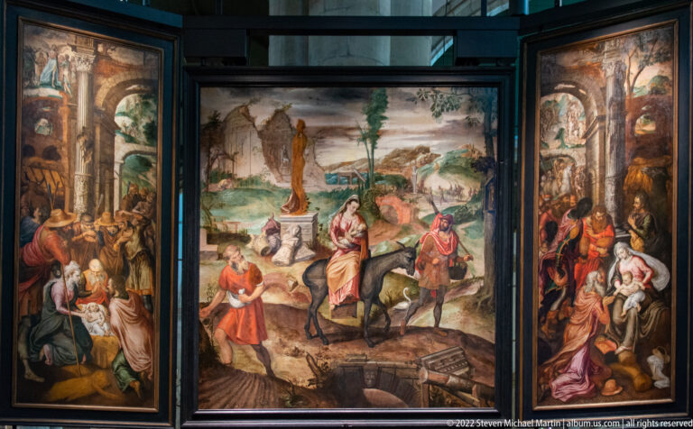 Painted triptych with a central landscape scene and crowded biblical narratives on both side panels.
