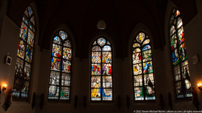 Four tall stained-glass windows glowing in a dark chapel-like interior of Sint-Janskerk.