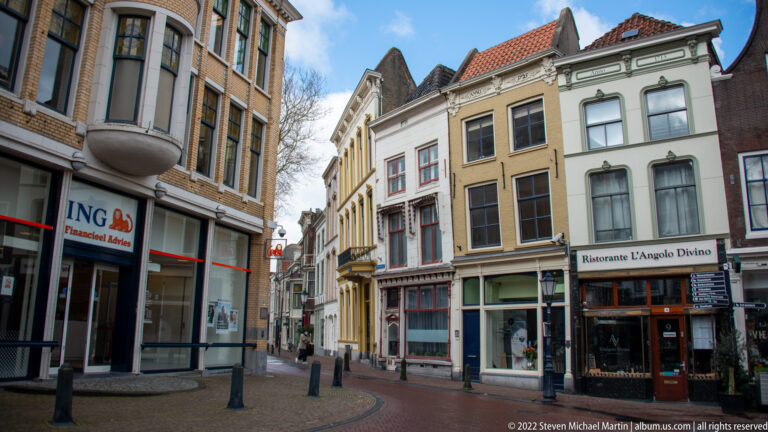 Narrow Gouda street lined with historic gabled buildings, shopfronts, and the restaurant L'Angolo Divino.