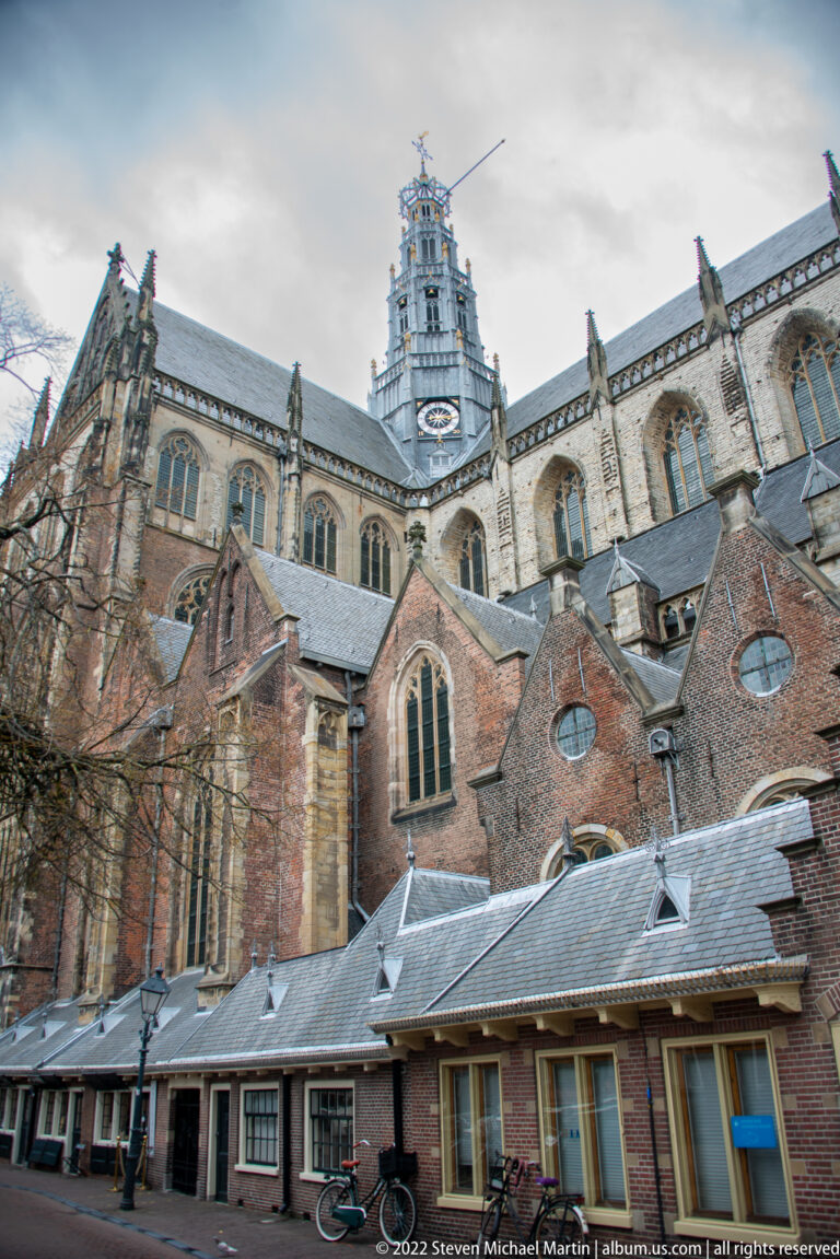 Oblique street-level view of Haarlem’s Grote or St.-Bavokerk with brick chapels, Gothic windows, and the openwork tower above.