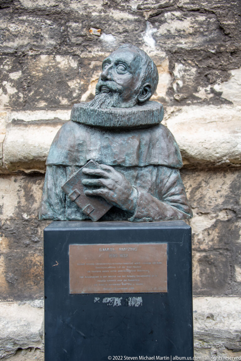 Small bronze bust of a man in historical dress on a dark stone plinth with a rectangular plaque.