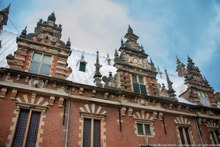 Upward view of the Vleeshal’s red-brick stepped gables, stone trim, sculptural details, and tall windows in Haarlem.