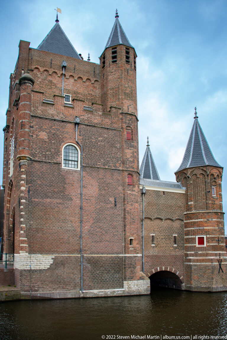 Waterside side of Amsterdamse Poort with tall brick walls, polygonal towers, and a low arched opening over the canal.