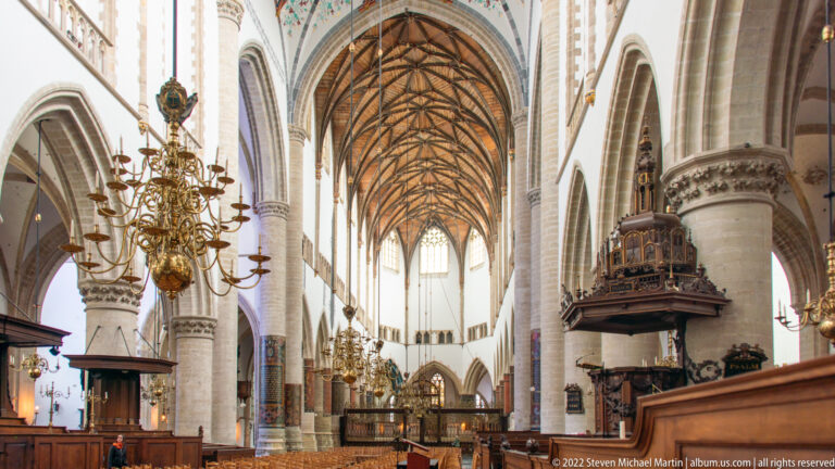 Side view inside Haarlem’s Grote Kerk with tall arcades, timber vault, brass chandelier, and carved pulpit.