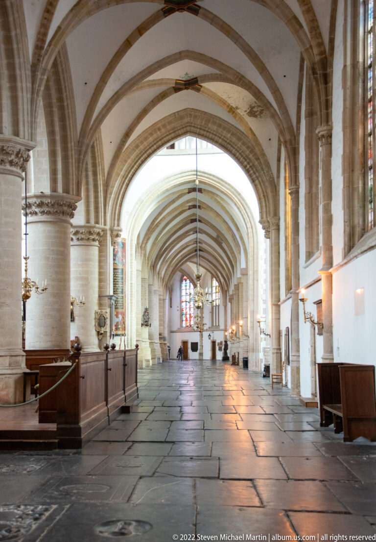 Long vaulted side aisle in Haarlem’s Grote Kerk with stone arches, wooden paneling, and ledger slabs in the floor.