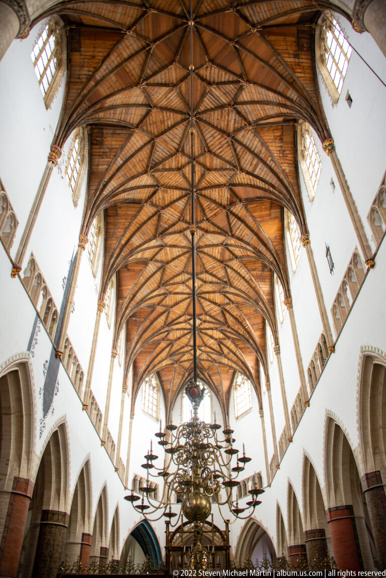 Upward view of the Grote Kerk’s timber nave roof with clerestory windows and a large brass chandelier below.