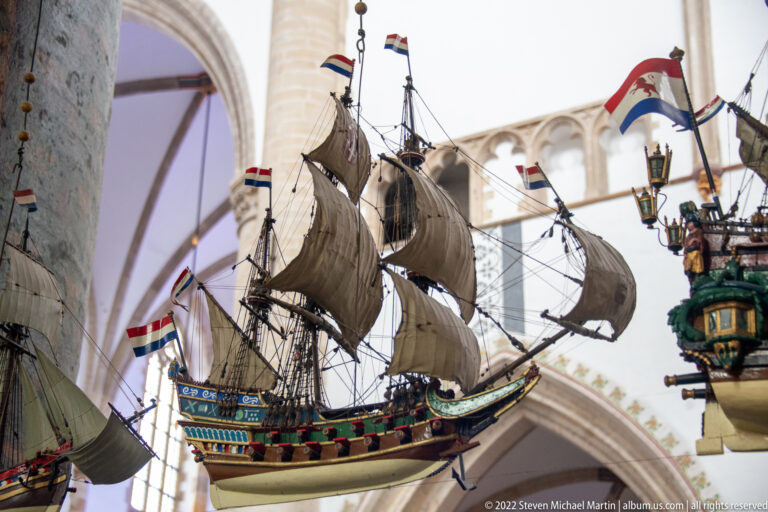 Suspended wooden sailing-ship model seen from below, with multiple set sails, rigging, painted hull, and Dutch flags.