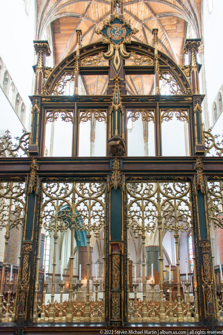 Frontal view of an ornate dark-painted and gilded choir screen with a central opening into the church choir.