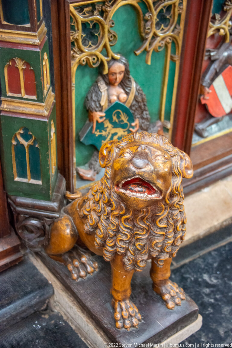 Polychrome carved lion with open mouth and curled mane at the base of an ornate church furnishing.