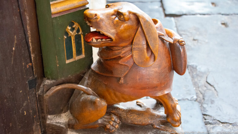 Brown carved dog with long ears and open mouth supporting or adjoining a painted church furnishing.