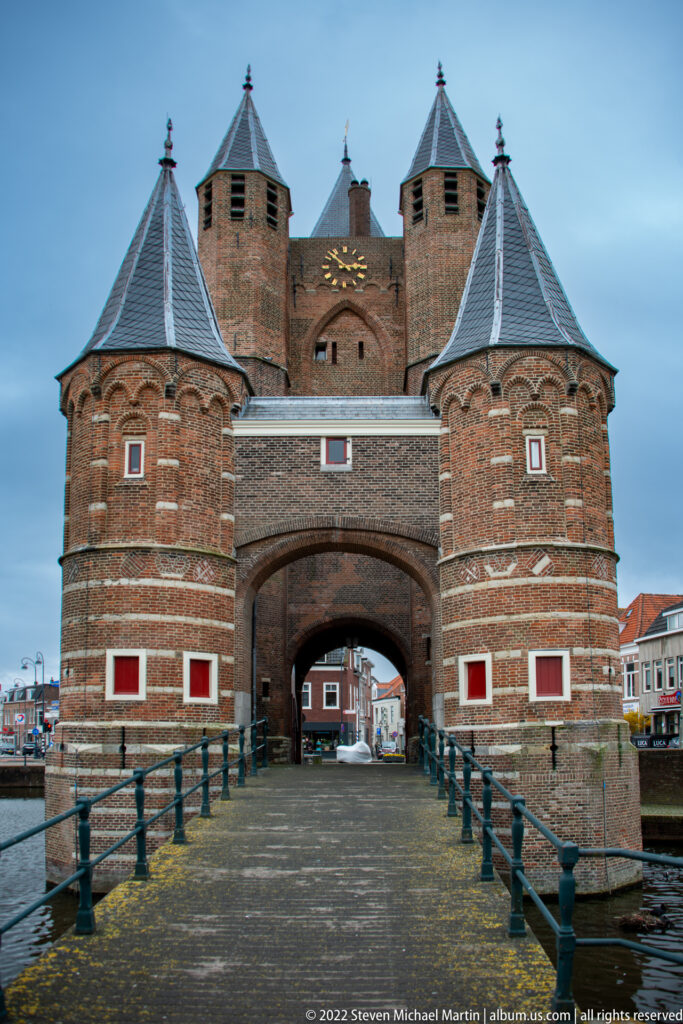 Symmetrical bridge approach to Amsterdamse Poort, with round flanking towers and a deep central arch.