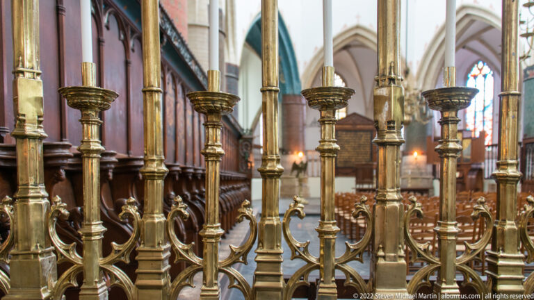 Close view of polished metal uprights and branching ornaments on a choir screen, with dark wooden stalls beyond.
