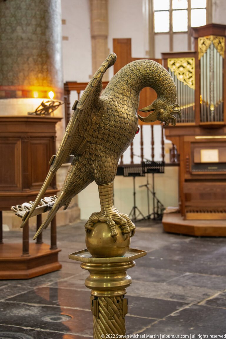 Metal eagle lectern with spread wings mounted on an ornate pedestal inside a church choir.