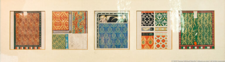 Wall display of narrow colorful pattern studies with geometric, floral, and scrolling motifs arranged in several framed groups.