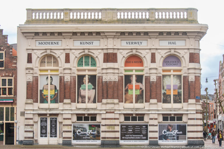Historic brick-and-stone exhibition building with arched windows, balustrade, and modern art graphics across the façade.